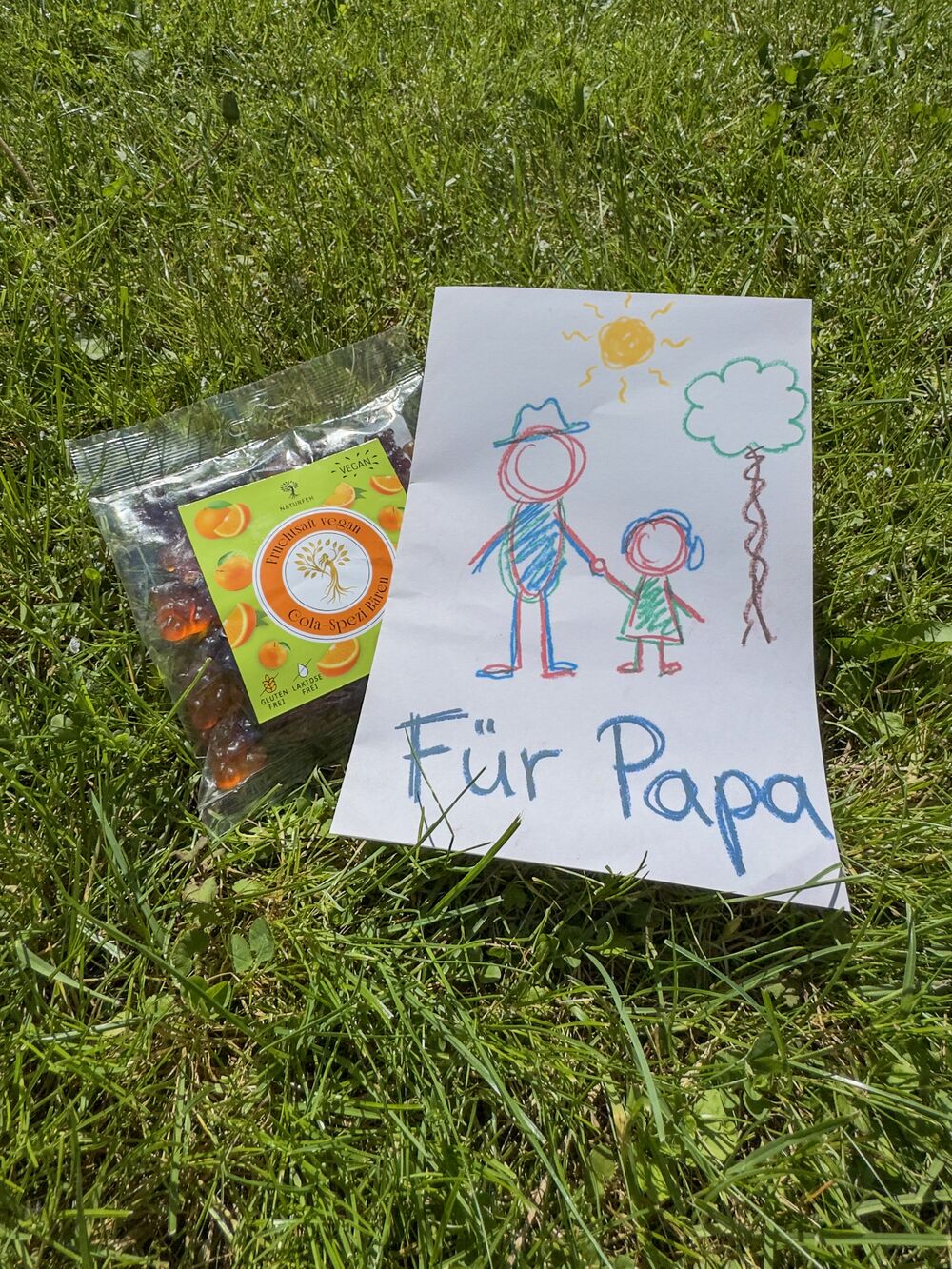 Kinderzeichnung Für Papa neben einer Tüte NATURFEH Fruchtgummi auf einer Wiese