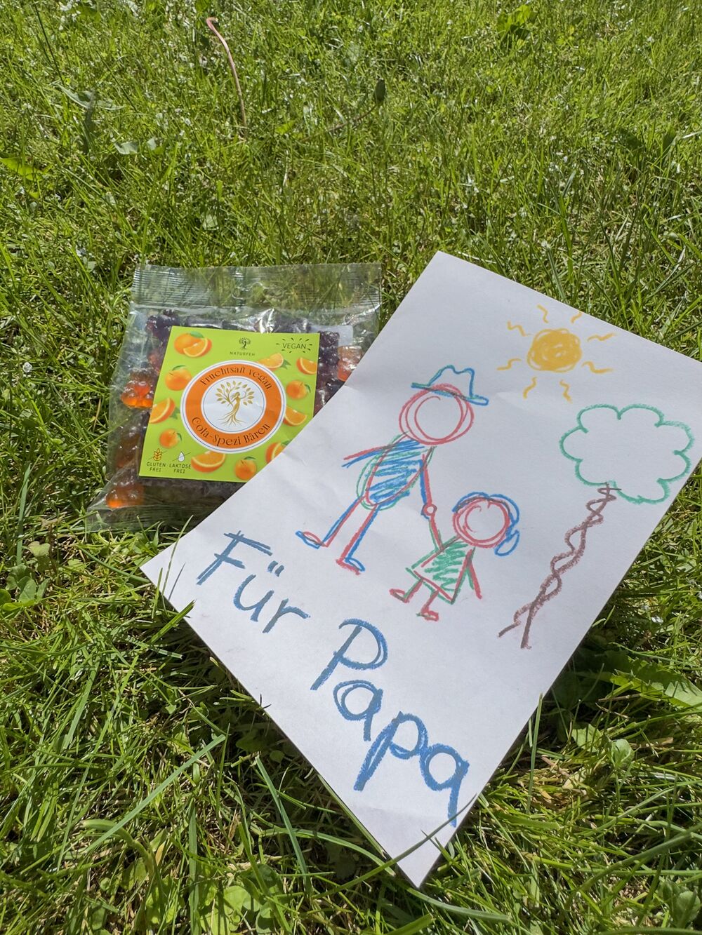 Kinderzeichnung Für Papa neben einer Tüte NATURFEH Fruchtgummi im Gras